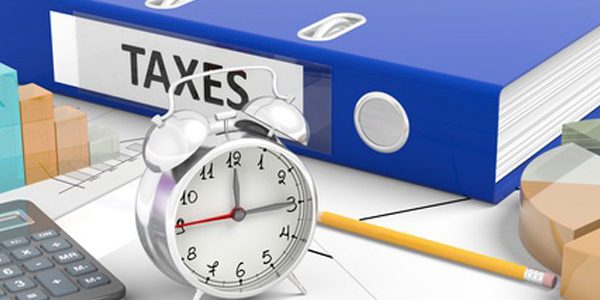 Clock with"Taxes" folder on busy office desk.