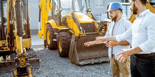 Builder choosing heavy machinery for construction with a sales consultant on the open ground of a shop with special vehicles